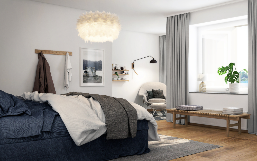 Ett sovrum inrett med en mörkblå säng och en lurvig taklampa. I fönstret hänger gardiner med lite grönska i fönstrena. 